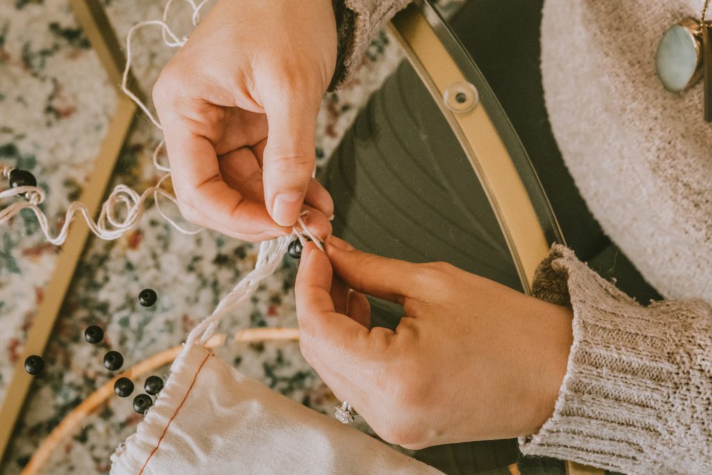 Hands putting together a modmala necklace with wooden beads
