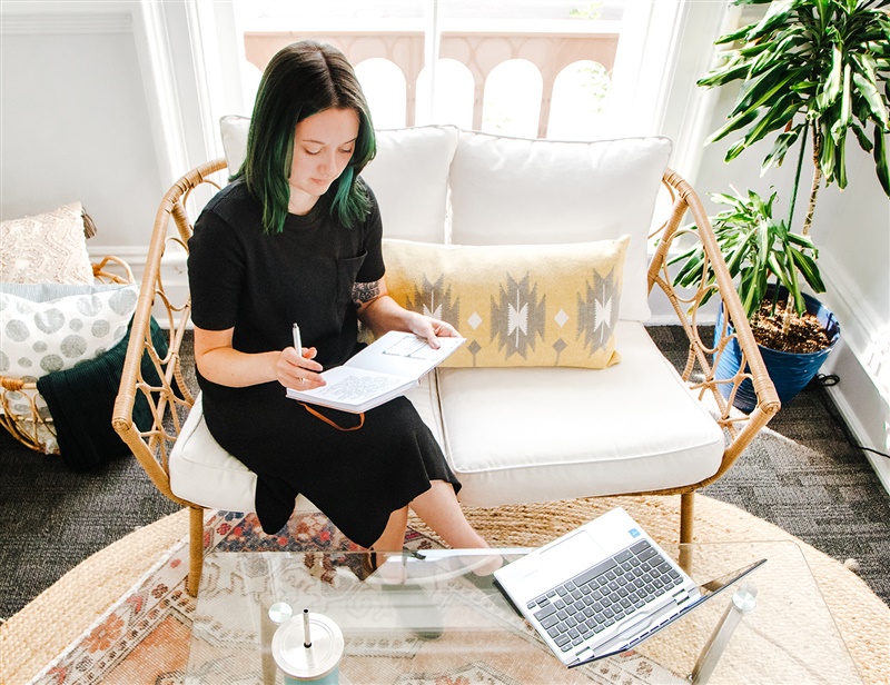 Jenna Brooks on wicker settee working on laptop